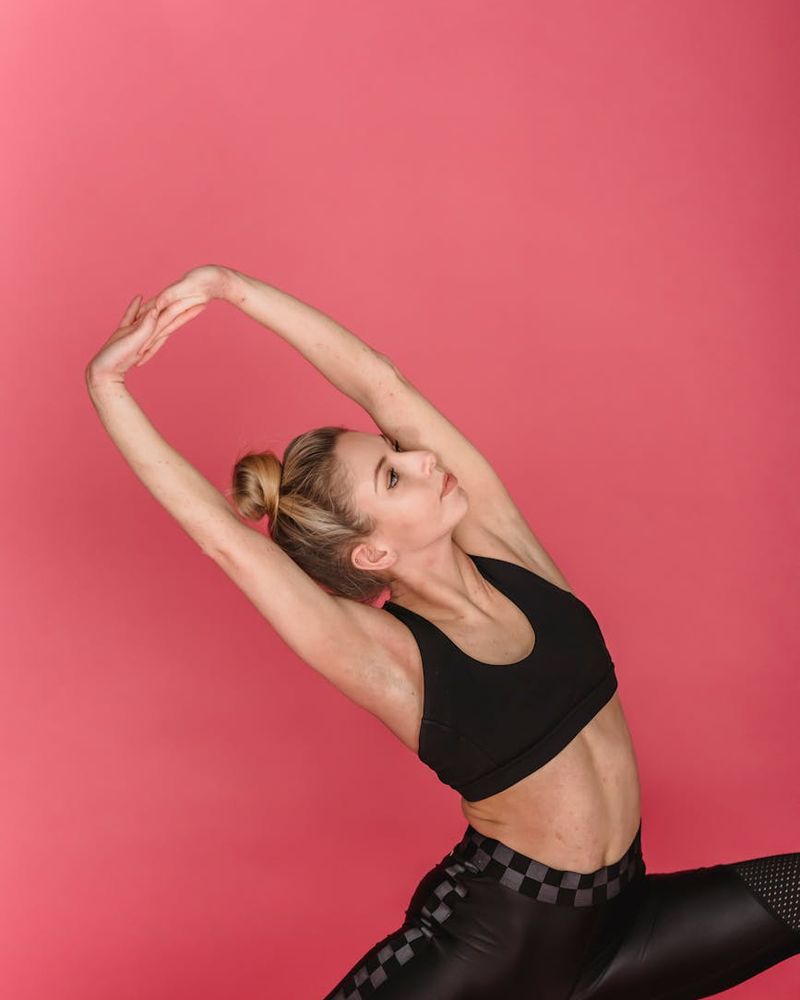 Young woman practicing deep flexibility yoga pose in soft pink lighting